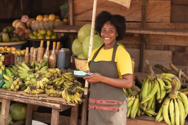 A fruit seller at her stall taking a digital payment on a POS device